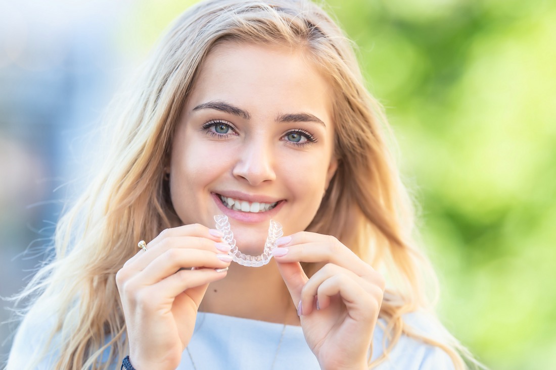 Foto einer lächelnden Patientin mit einer transparenten Zahnschiene von Invisalign in den Händen