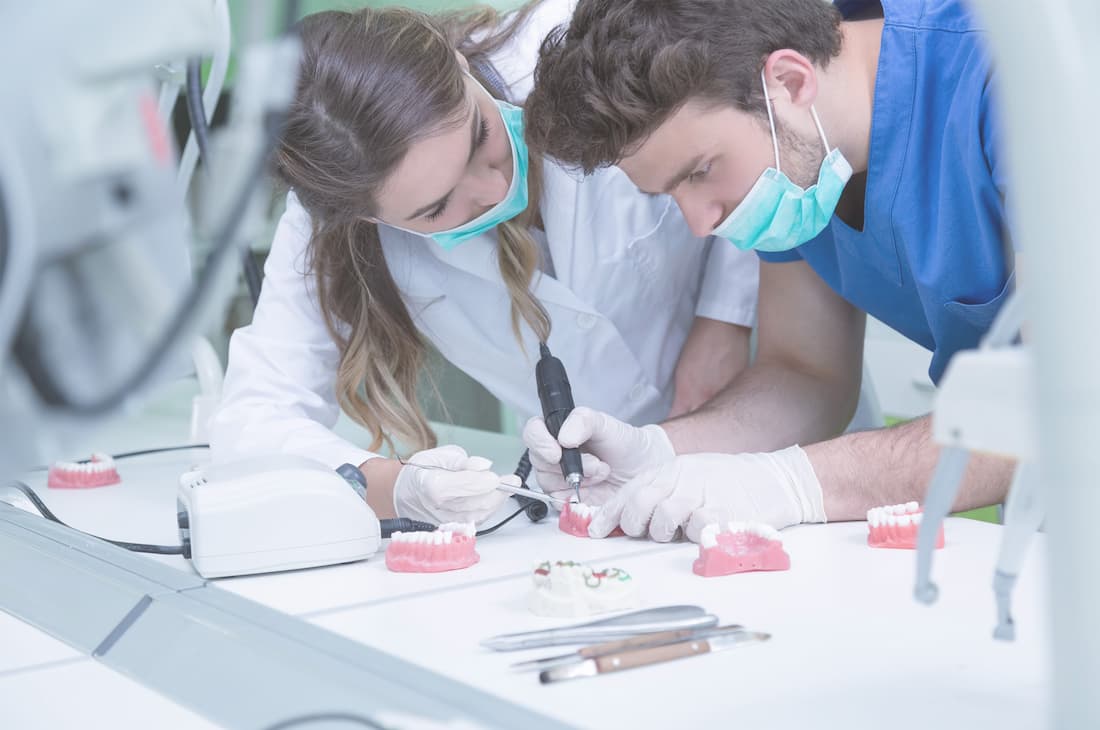 Zahntechniker und Zahntechnikerin bei der Arbeit mit einem Handfräser im Dentallabor